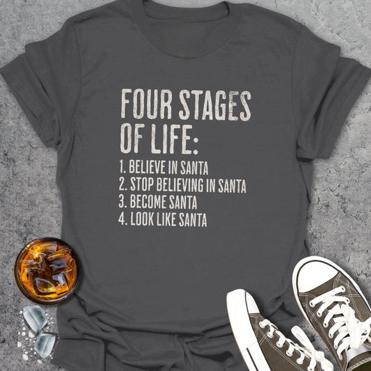 Gray t-shirt with 'Four Stages of Life' text, placed on a textured surface with a glass of whiskey and sneakers.